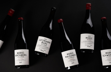 Sechs Weinflaschen vor schwarzem Hintergrund, etiketiert in elegantem, minimalistischen Design.