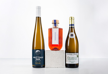 Drei edle Flaschen auf weißem Hintergrund; links und rechts Wein, in der Mitte Negroni.