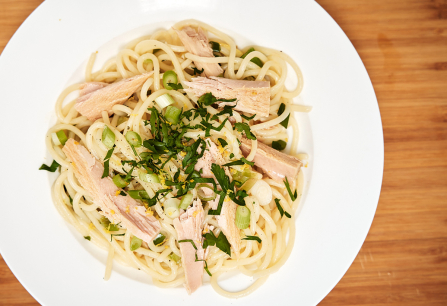 Spaghetti mit Thunfisch, Frühlingszwiebeln und Petersilie auf weißem Teller.
