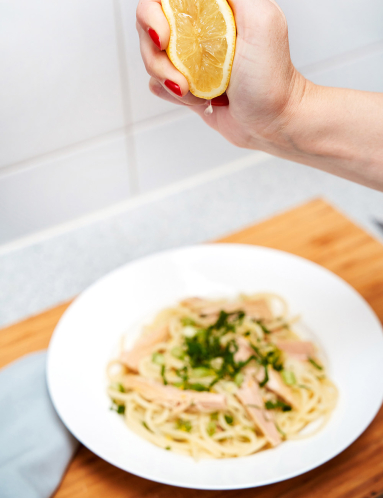 Zitrone wird über einem Teller mit Nudeln und Kräutern ausgepresst.