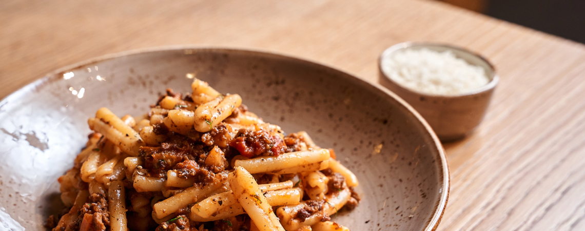 Rustikale Schüssel mit Pasta und Fleischsoße, daneben kleine Schale mit Parmesan.