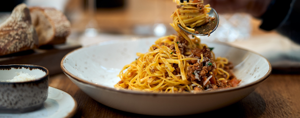Teller mit Spaghetti Bolognese, nah aufgenommen, daneben Brot und geriebener Käse.