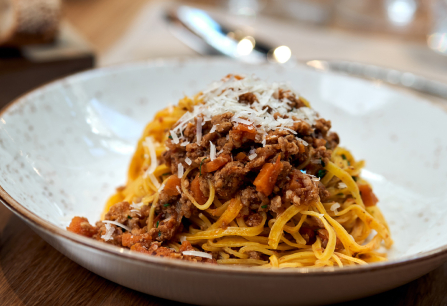 Spaghetti Bolognese mit geriebenem Käse auf einem weißen Teller, im Restaurant serviert.