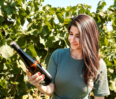 Frau in grünem Kleid hält Weinflasche vor grünem Weinberg.