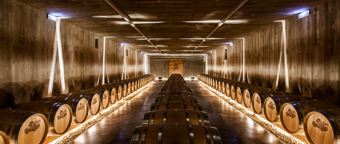 Holzfasskeller mit warmem Licht und symmetrischer Anordnung der Fässer.