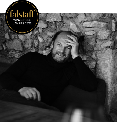 Schwarz-weiß-Porträt eines Mannes in Dunkelkleidung vor einer Steinwand.