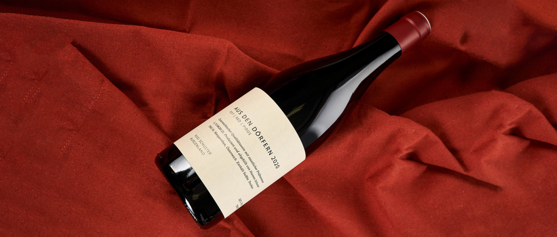 Rotweinflasche mit Etikett auf rotem Stoffhintergrund.