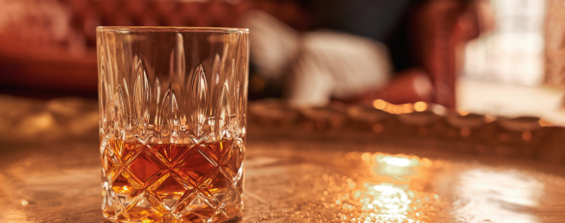 Kristallglas mit goldenem Getränk auf kunstvoll verziertem Tablett im Wohnzimmer.