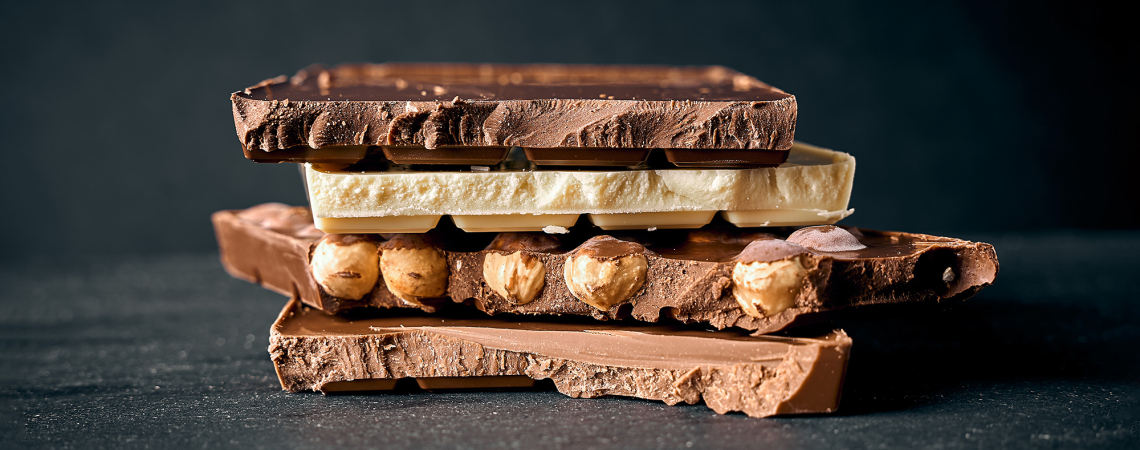 Drei Schokoladensorten mit Nüssen gestapelt auf dunklem Hintergrund.