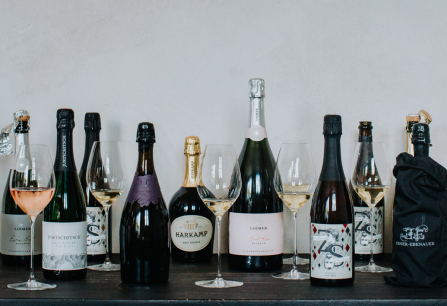 Verschiedene Sektflaschen und Gläser mit Sekt auf einem dunklen Tisch.