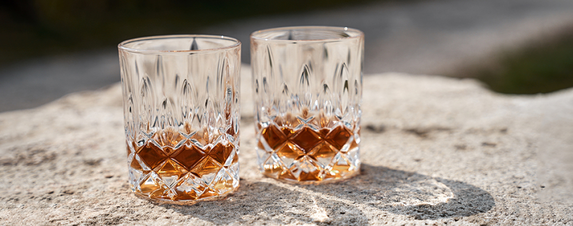 Zwei befüllte Kristallgläser mit geometrischem Schliff auf einer Steinoberfläche.