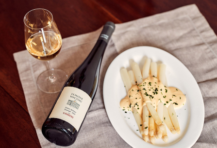 Weißwein neben Spargel mit Sauce auf weißem Teller, Holzuntergrund.