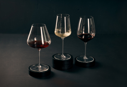 Drei Weingläser mit Rot- und Weißwein auf dunklem Hintergrund, stilvoll präsentiert.