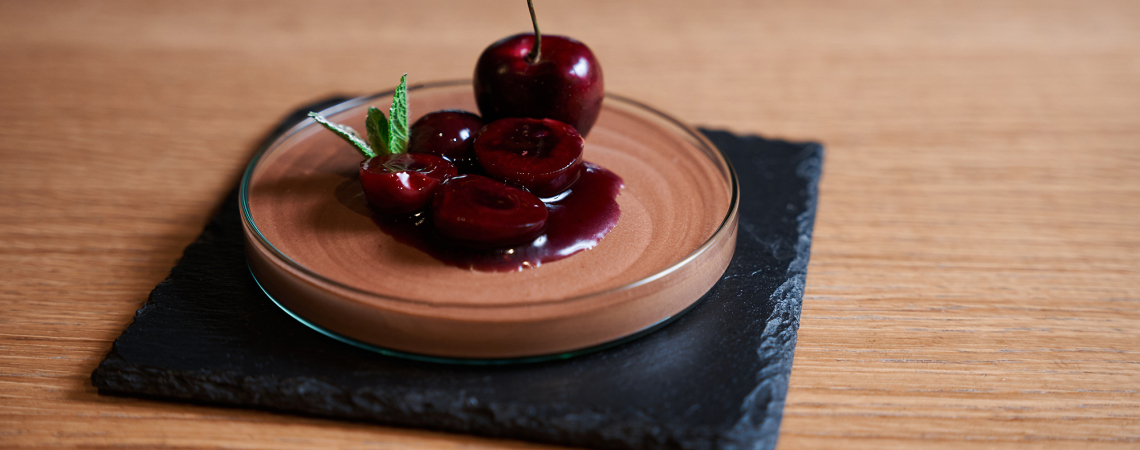 Schokoladenmousse im Glas mit Kirschen und Minze auf Schieferplatte.