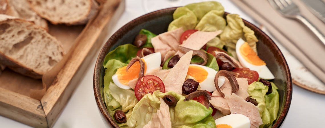 Grüner Salat mit Eiern, Tomaten, Oliven und Thunfisch, daneben frisches Brot.