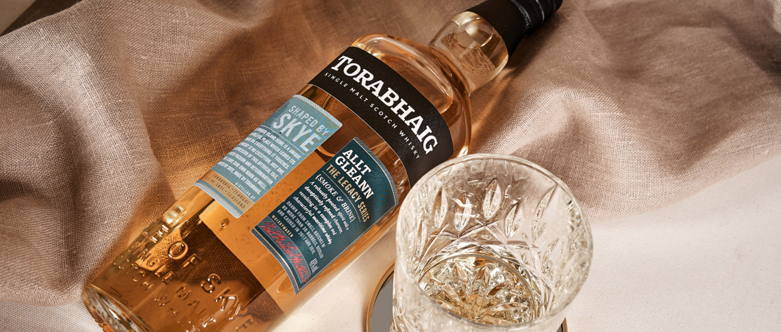 Whiskyflasche und Glas auf beigem Stoff drapiert, elegantes, edles Erscheinungsbild.