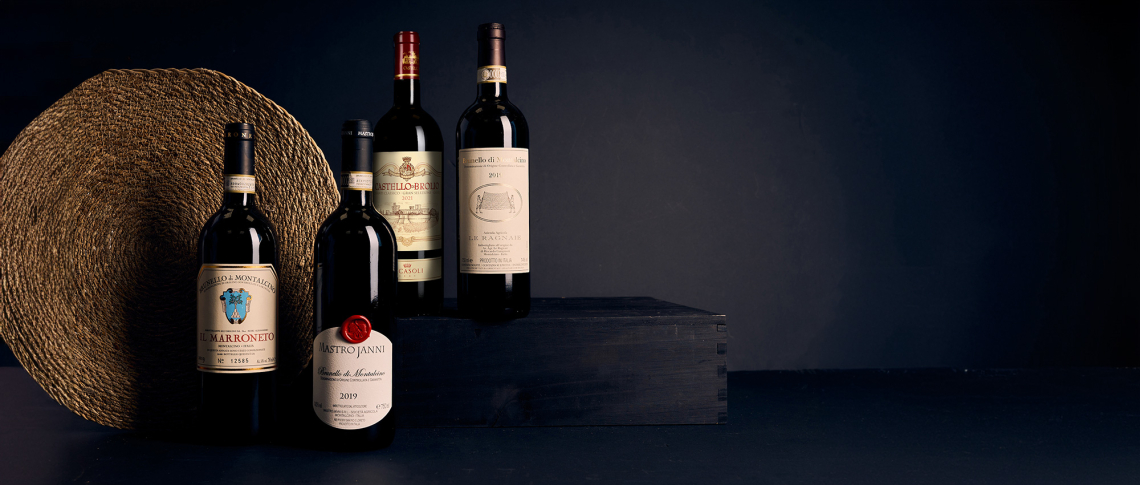 Vier Weinflaschen auf dunklem Hintergrund, teilweise auf Holzbox drapiert.