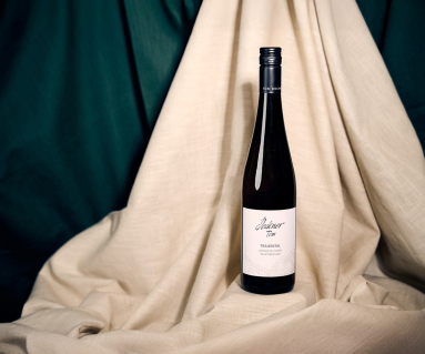 Weinflasche vor beigem und grünem Stoffhintergrund elegant inszeniert.