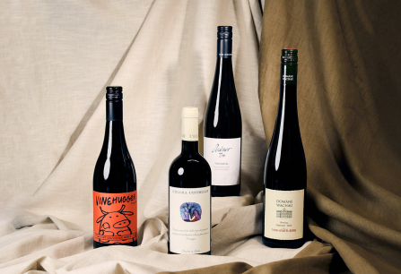 Vier Weinflaschen arrangiert auf beigem Stoffhintergrund.