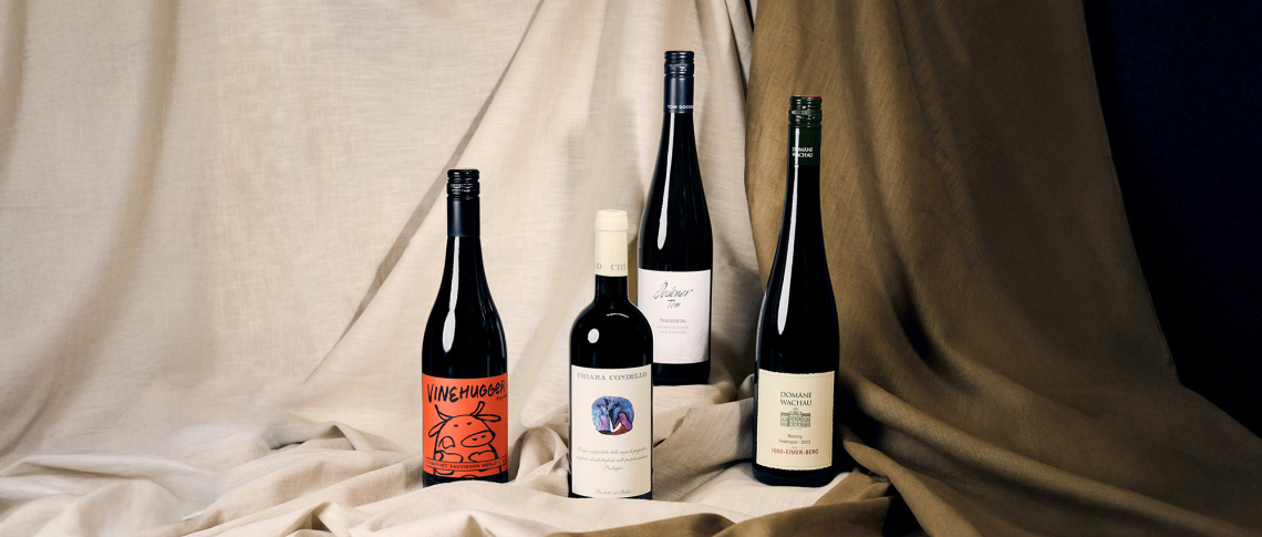 Vier Weinflaschen arrangiert auf beigem Stoffhintergrund.