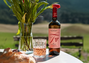 Flasche und Glas Roséwein auf Tisch, umgeben von Natur und Blumen.