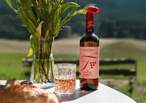 Flasche und Glas Roséwein auf Tisch, umgeben von Natur und Blumen.