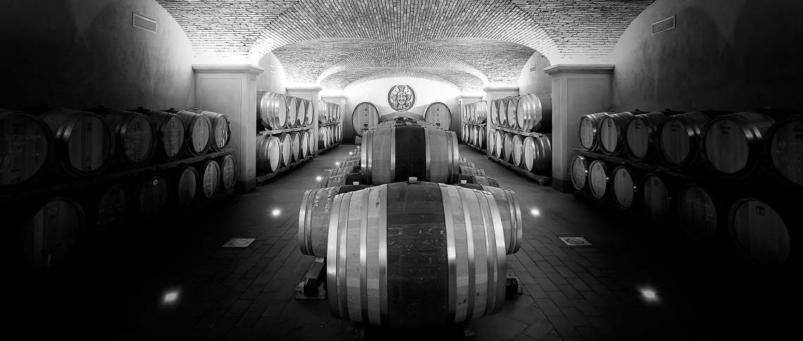 Schwarz-weiß-Foto eines Weinkellers mit gestapelten Holzfässern und Gewölbedecke.