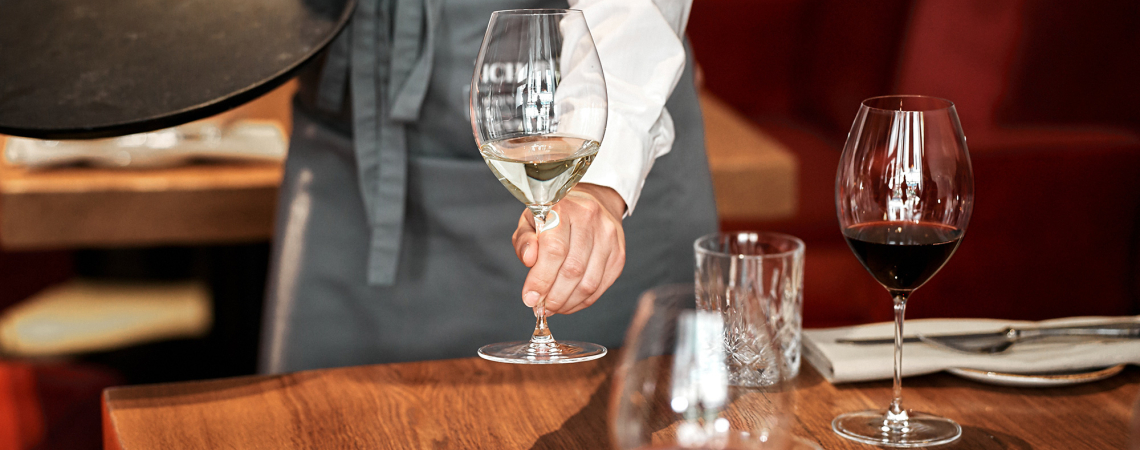 Kellner serviert Getränk in modernem Restaurant, mit elegant gedecktem Holztisch.