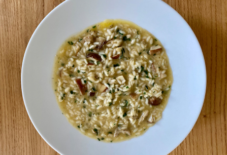 Cremiges Pilzrisotto auf weißem Teller, auf hölzernem Tisch serviert.