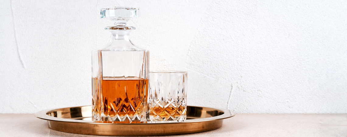 Kristallkaraffe und Glas mit Getränk auf goldenem Tablett vor hellem Hintergrund.