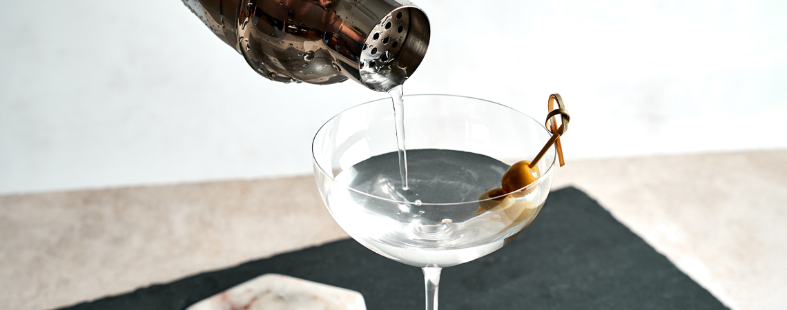 Cocktail mit Olive wird in ein elegantes Martiniglas gegossen.