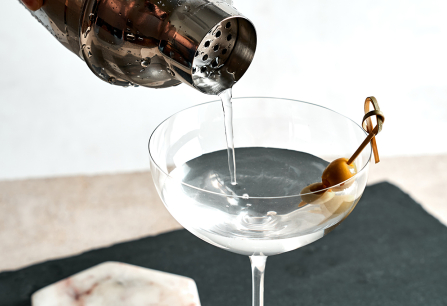 Cocktail mit Olive wird in ein elegantes Martiniglas gegossen.