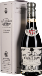 Eine elegante Flasche Balsamico-Essig mit schwarzem Glas, verziert mit traditionellen Emblemen und Schriftzügen in Weiß und Silber. Sie befindet sich vor einer passenden, stilvollen Verpackungsbox in gedeckten Farben, ebenfalls mit dekorativen Mustern und