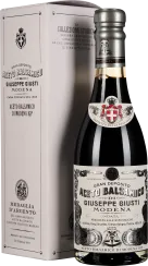 Eine elegante Flasche Balsamico-Essig mit schwarzem Glas, verziert mit traditionellen Emblemen und Schriftzügen in Weiß und Silber. Sie befindet sich vor einer passenden, stilvollen Verpackungsbox in gedeckten Farben, ebenfalls mit dekorativen Mustern und