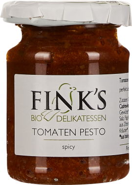 Glas mit rotem Tomatenpesto, beschriftet als Delikatesse. Das Pesto erscheint grobkörnig und dickflüssig. Der Deckel ist weiß und wirkt leicht zerknittert.