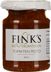 Glas mit rotem Tomatenpesto, beschriftet als Delikatesse. Das Pesto erscheint grobkörnig und dickflüssig. Der Deckel ist weiß und wirkt leicht zerknittert.