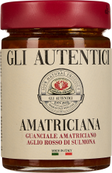 Das Bild zeigt ein Glas mit rotem Deckel, gefüllt mit einer roten Sauce. Das Etikett ist cremefarben mit schwarzer und roter Schrift. Ein stilisiertes Emblem in der Mitte enthält ein rotes Logo. Darunter verläuft ein grüner, weißer und roter Streifen, sim