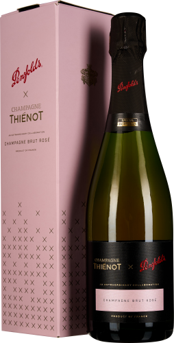 Flasche mit goldenem Glanz, verziert mit schwarzem Etikett und rotem Schriftzug, neben einer rosa Geschenkbox mit dezentem Muster.