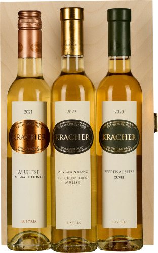 Drei Weinflaschen in einer Holzbox, jede mit einem metallischen Schraubverschluss in Rotgold, Gold und Dunkelgrün. Etiketten sind in elegantem Design gestaltet. Die Flaschen enthalten unterschiedliche Jahrgänge.