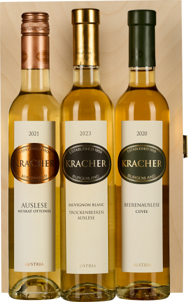 Drei Weinflaschen in einer Holzbox, jede mit einem metallischen Schraubverschluss in Rotgold, Gold und Dunkelgrün. Etiketten sind in elegantem Design gestaltet. Die Flaschen enthalten unterschiedliche Jahrgänge.