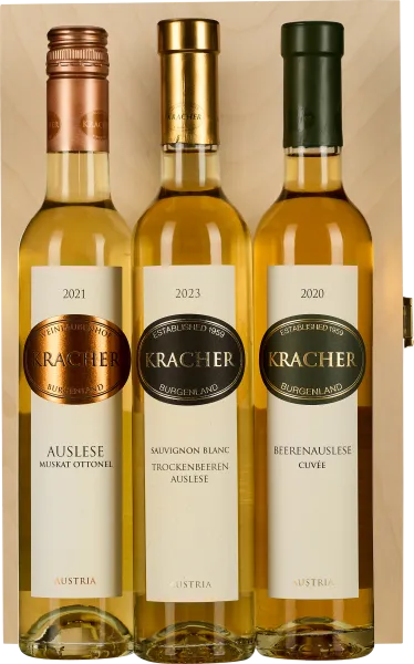 Drei Weinflaschen in einer Holzbox, jede mit einem metallischen Schraubverschluss in Rotgold, Gold und Dunkelgrün. Etiketten sind in elegantem Design gestaltet. Die Flaschen enthalten unterschiedliche Jahrgänge.