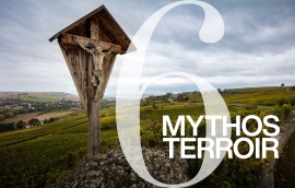 Holzkruzifix auf Hügel mit Weinbergen im Hintergrund unter bewölktem Himmel.