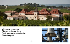 Historisches Gebäude mit Glockenspiel und roten Dächern, eingebettet in grüne Weinberge.