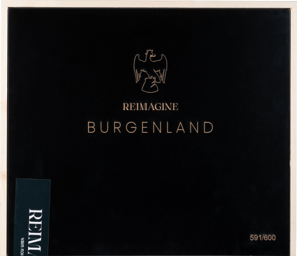 Schwarzer Kasten mit goldener Aufschrift und Adlermotiv auf Holzhintergrund.