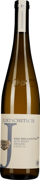 Eine schlanke, braune Weinflasche mit einer weißen Etikettierung, die einen eleganten, minimalistischen Stil zeigt. Die Flasche ist von einem schlichten metallischen Emblem und einem großen, stilisierten Buchstaben in der Mitte des Etiketts geziert.