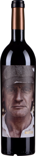 Dunkle Weinflasche mit einem auffälligen Etikett, das das Porträt eines älteren Mannes mit Schiebermütze zeigt. Kupferfarbener Flaschenverschluss, schlichtes Design.