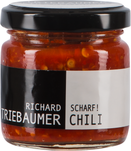 Kleines Glas mit schwarzem Deckel, gefüllt mit leuchtend roter, stückiger Chilipaste. Das Etikett ist zweifarbig, schwarz auf der linken und weiß auf der rechten Seite.