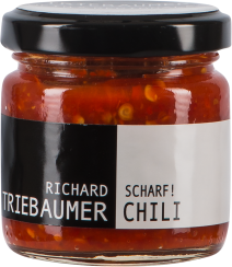 Kleines Glas mit schwarzem Deckel, gefüllt mit leuchtend roter, stückiger Chilipaste. Das Etikett ist zweifarbig, schwarz auf der linken und weiß auf der rechten Seite.