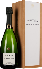 Grüne Sektflasche mit schwarzem Verschluss, etikettiert, daneben eine elegante, hölzerne Geschenkbox mit weißem Deckel.