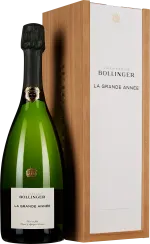 Grüne Sektflasche mit schwarzem Verschluss, etikettiert, daneben eine elegante, hölzerne Geschenkbox mit weißem Deckel.